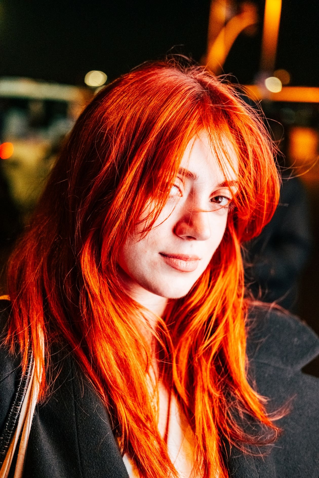 Smiling woman with striking red hair and a confident look at night