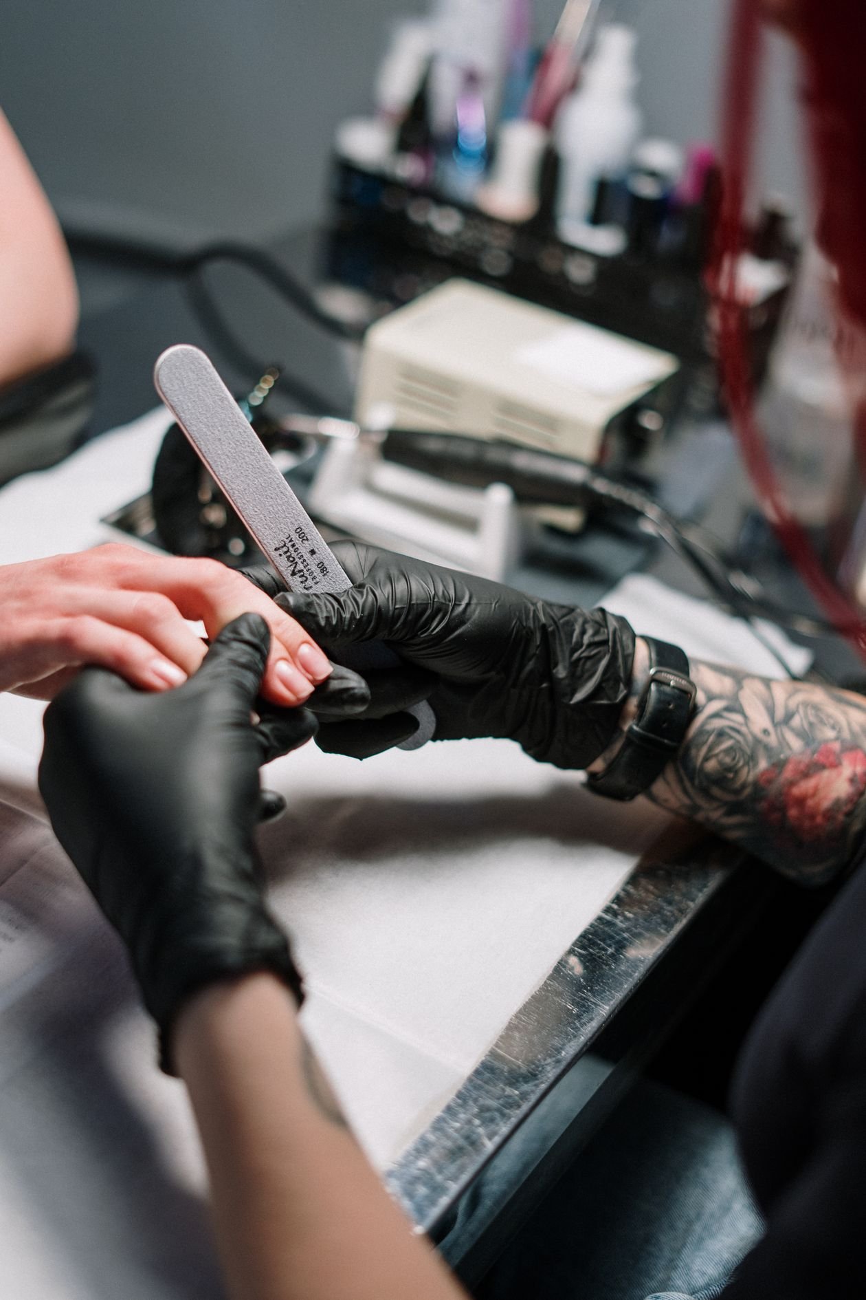 Manicurist wearing black gloves filing a client's nails in a beauty salon